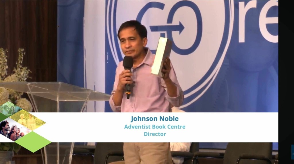 Johnson T. Noble, Adventist Book Centre Director, speaking and holding a book