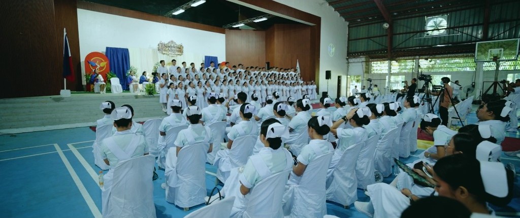 Nursing students seated in the gymnasium facing classmates on stage