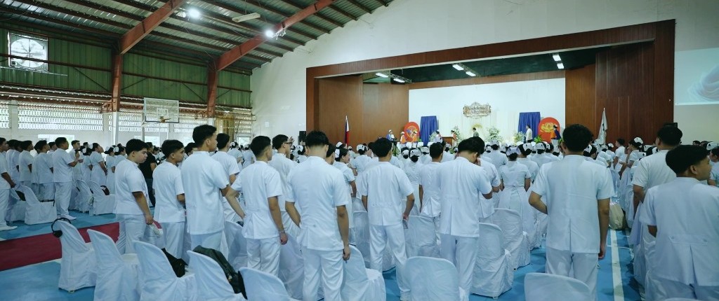 Nursing students in white uniforms fill the gymnasium during the ceremony