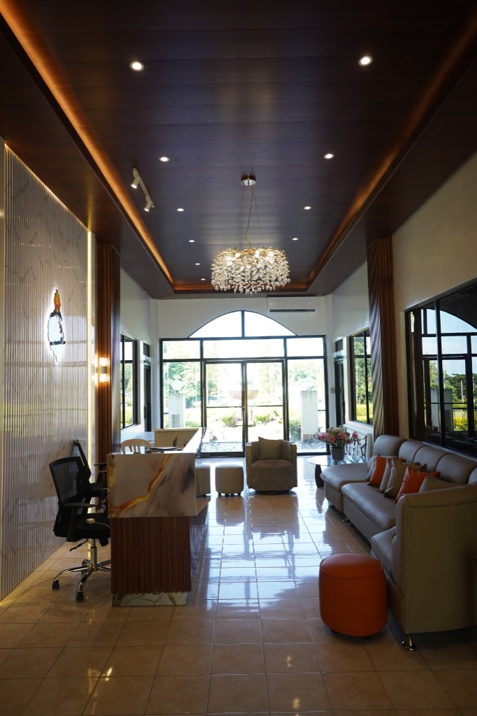 The student lounge with reception desk, seating, chandelier lighting, and garden views through arched windows