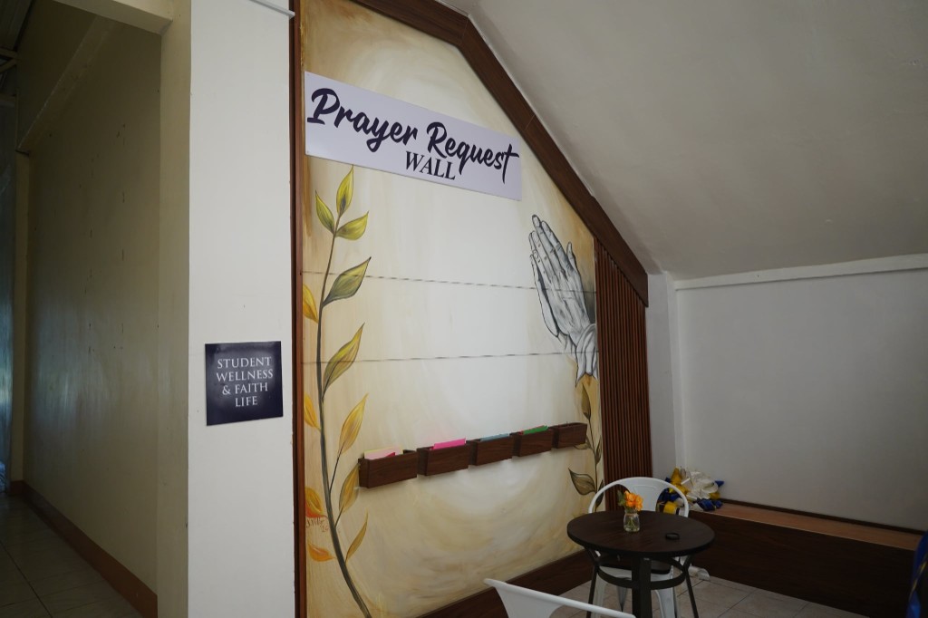 The Prayer Request Wall with praying hands mural, note pockets, and a Student Wellness and Faith Life sign